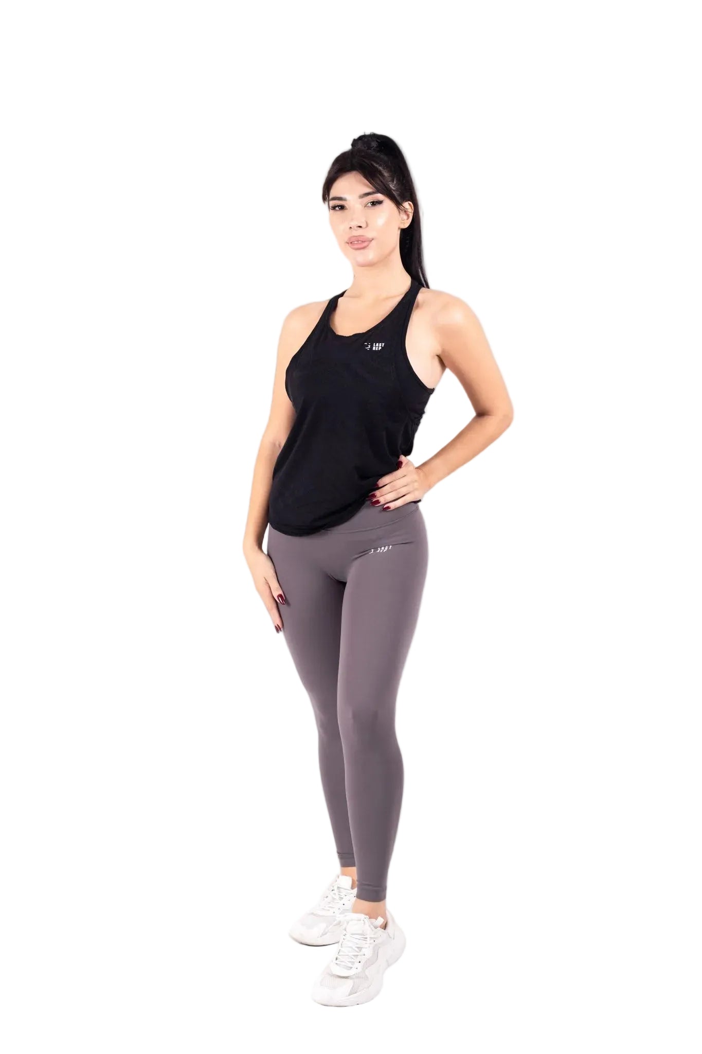 A woman wearing a black tank top with built-in sports bra and gray leggings, standing against a white background.