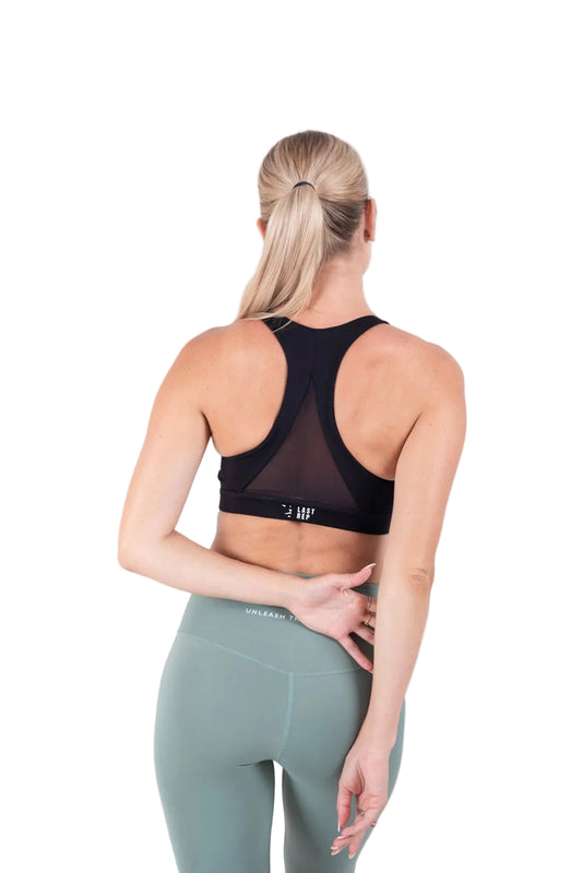 Person wearing a black sports bra and green leggings on a gray background