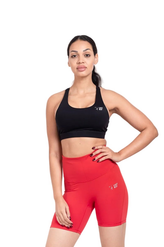 Woman wearing a black sports bra and red shorts on a white background